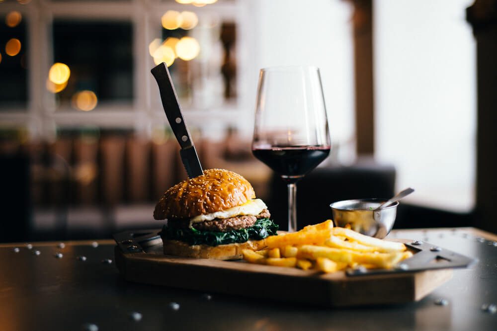  Burger Placed on a Table Next to Glass of Red Wine and Fries 