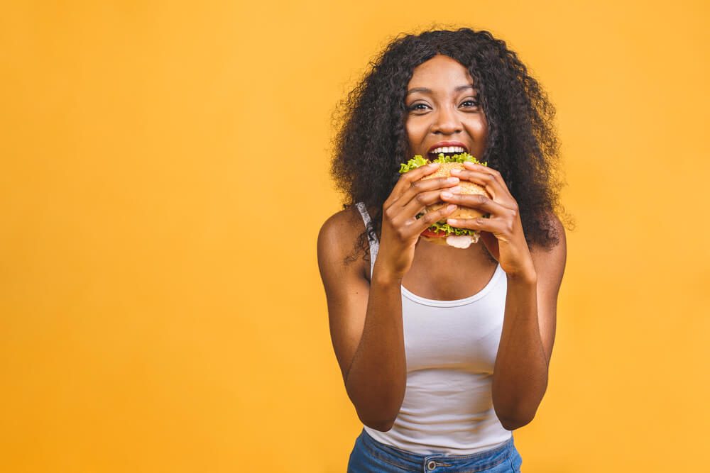 African American Black Beautiful Young Woman Eating Hamburger Isolated on Yellow Background