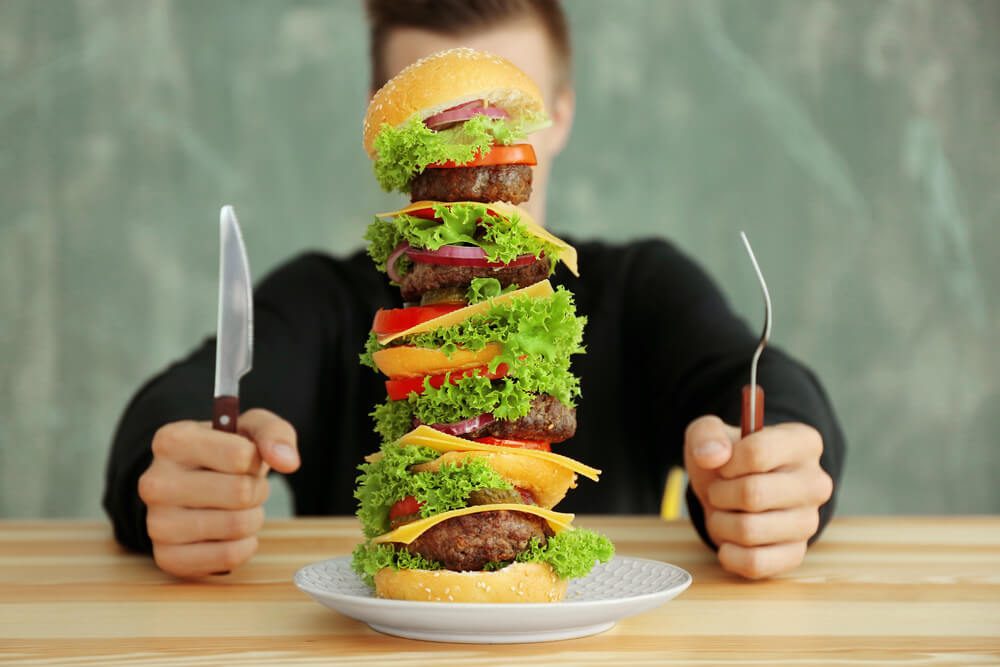 Man Eating Huge Burger at Table