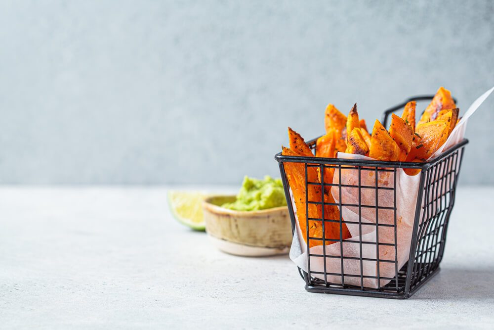 Fried Sweet Potato Wedges in a Metal Basket, Gray Background. Vegan Food Concept.