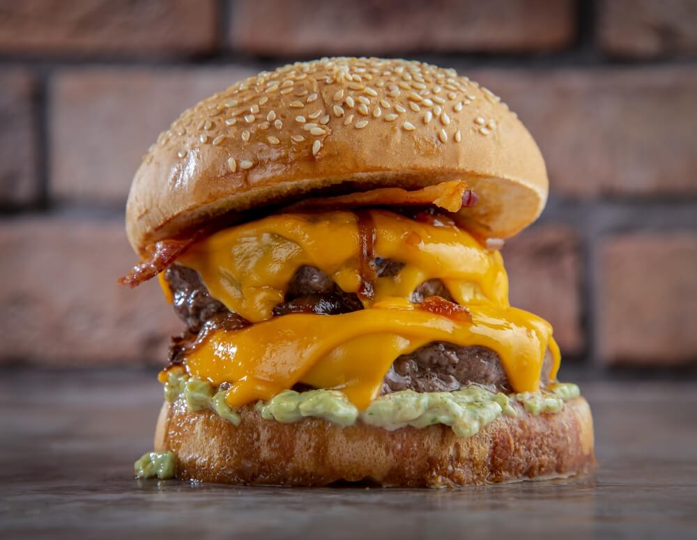 Double Cheese Burger Sandwich With Some Melted Cheddar Cheese Onion Lettuce Placed Isolated on the Center of a Wooden Surface and Brick Texture Background