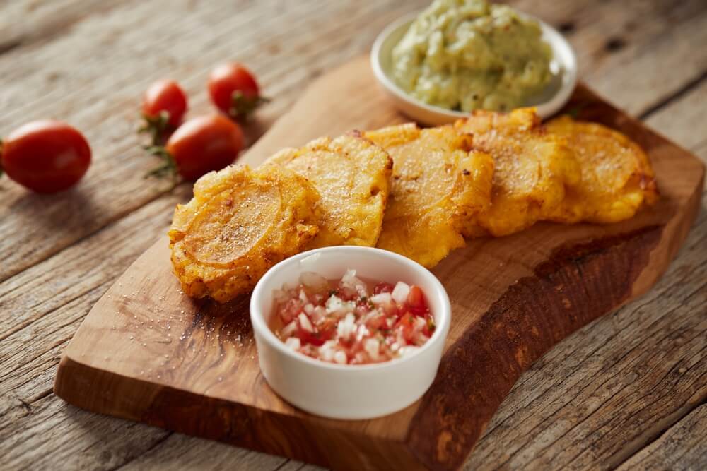 Tostones accompanied with guacamole and served on a traditional plate with a wooden and rustic background